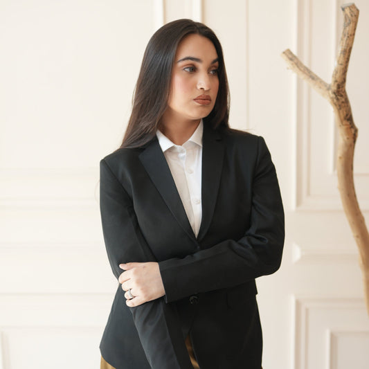Woman in a black suit and white shirt posing with a branch indoors.