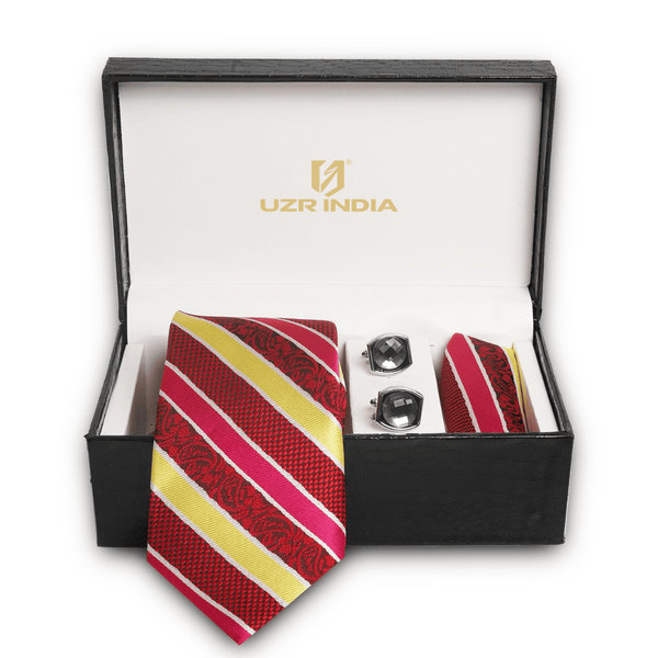 A men's formal accessory gift set in an open black presentation box. The set includes a striped red, pink, and yellow necktie, matching pocket square, and two silver cufflinks.